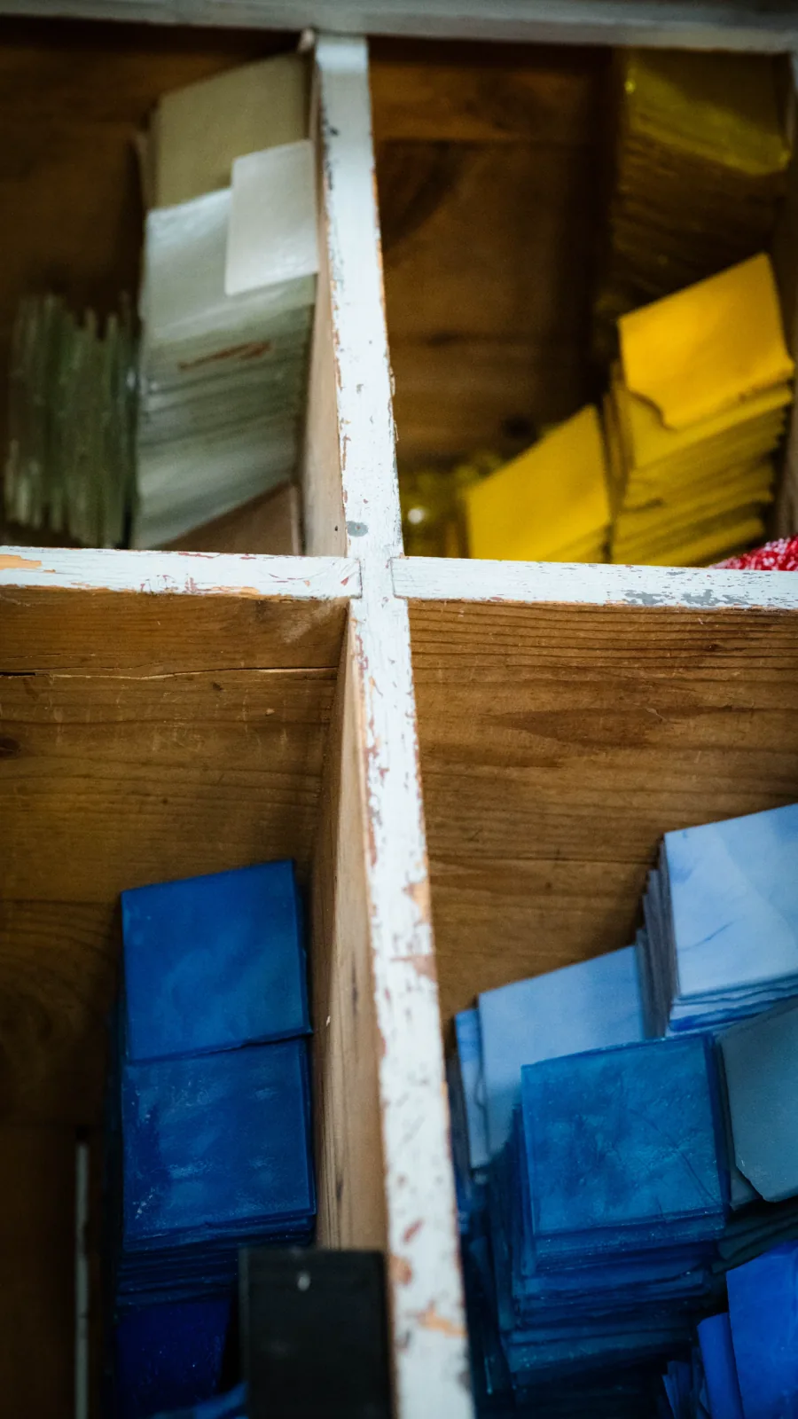 Casier de tesselles en pâte de verre bleues, jaunes et blanches dans l'atelier